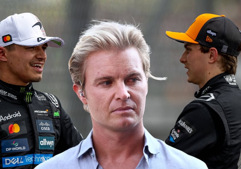 Lando Norris and Oscar Piastri look at one another with a scowling Nico Rosberg between them