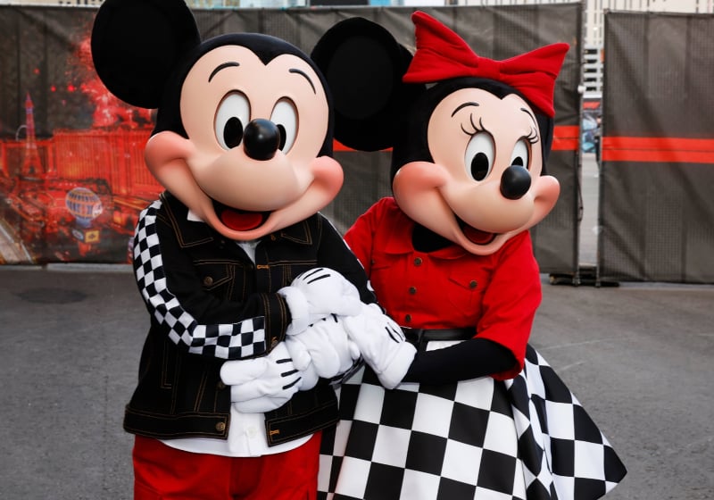 Lifesize Mickey and Minnie Mouse characters facing the camera holding hands in the F1 Las Vegas GP paddock.