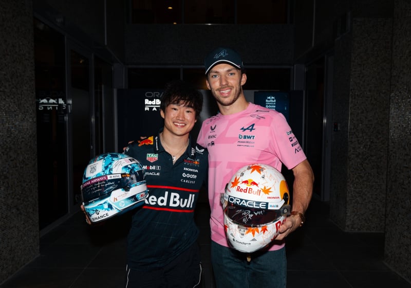 Yuki Tsunoda and Pierre Gasly smiling at the camera after their helmet swap at the Abu Dhabi Grand Prix 2025