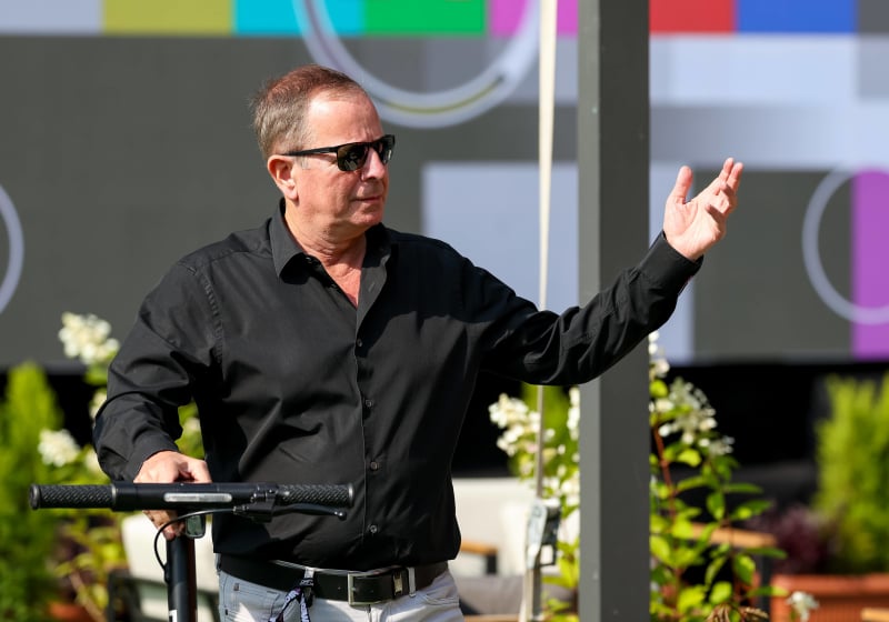 Martin Brundle wheels a bike and gesticulates with his hand looking into the distance, somewhat annoyed