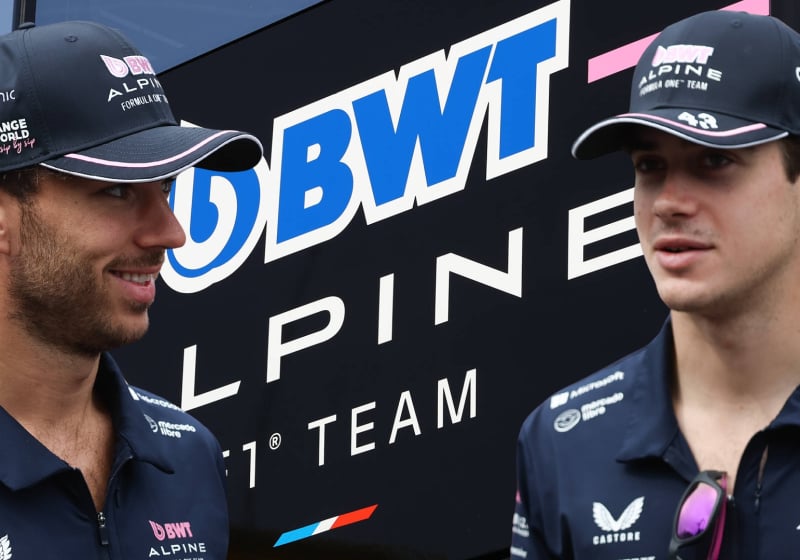 Pierre Gasly and Franco Colapinto look at each other to the background of an Alpine logo