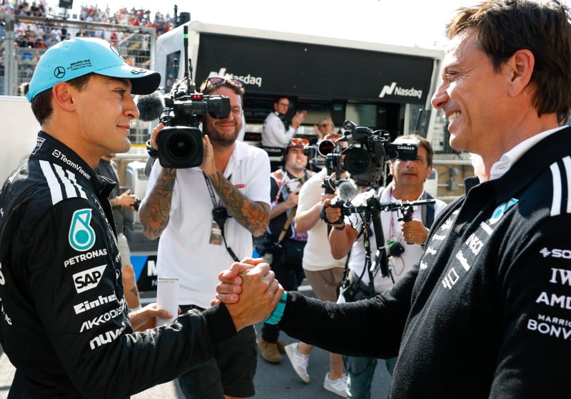Russell shaking hands with Mercedes boss Wolff at F1 track, both smiling