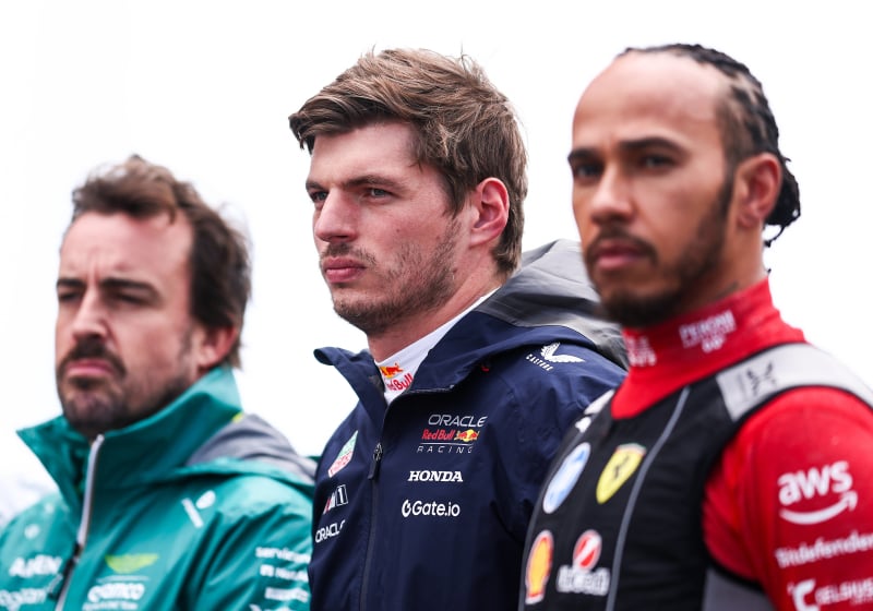 Max Verstappen and Fernando Alonso stand next to Lewis Hamilton